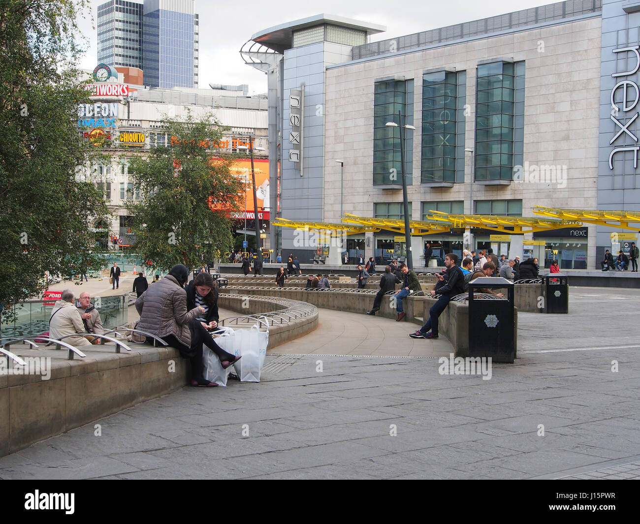 Exchange Square dans le centre de Manchester, Angleterre, montrant des gens assis, d'attente et de détente avec la station de tramway coloré dans la b/g. Banque D'Images