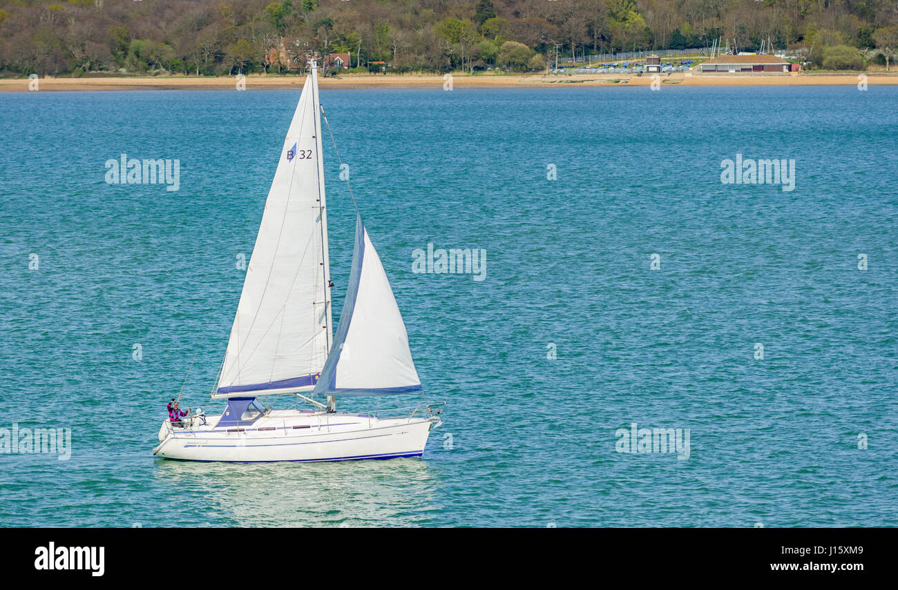 Petit yacht blanc. Petit yacht à voiles voile jusqu'à un étroit bras d'eau près de la mer, avec terrain Solent montrant derrière le yacht. Banque D'Images