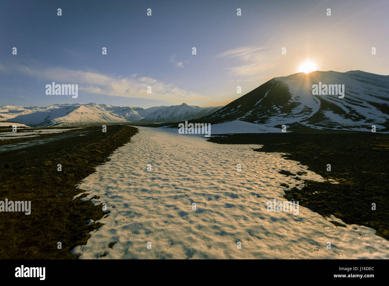 Soleil se couche derrière les montagnes enneigées dans le champ de lave de Berserkjahraun (Snæfellsnes, péninsule de Snæfellsnes), dans l'ouest de l'Islande Banque D'Images