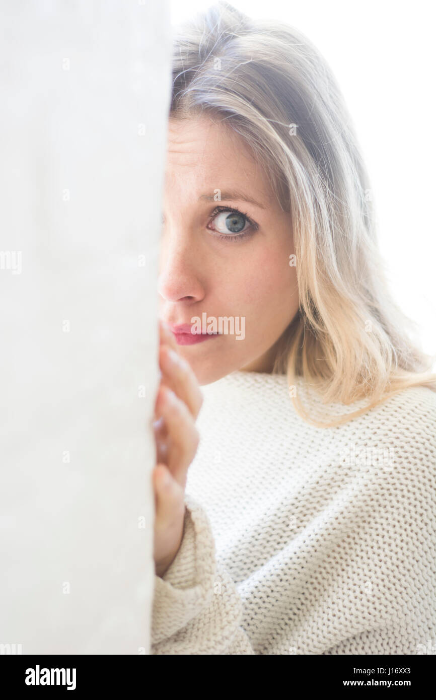 Jeune femme blonde se cacher derrière le mur Banque D'Images
