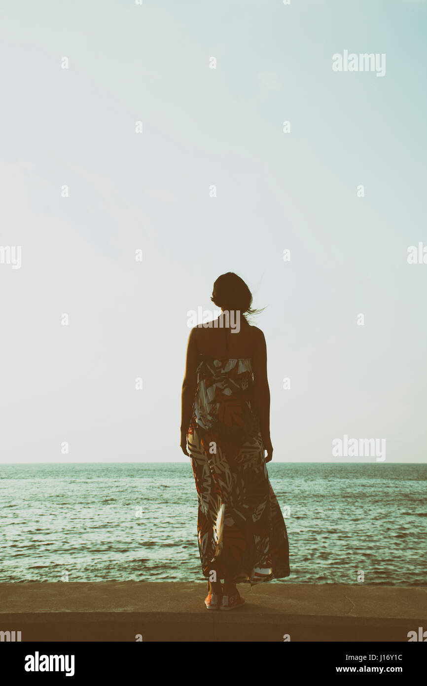 Vue arrière d'une jeune femme portant une robe d'été debout près de la mer Banque D'Images