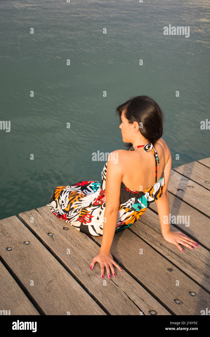 Vue arrière d'une jeune femme était assise sur le quai par la mer Banque D'Images