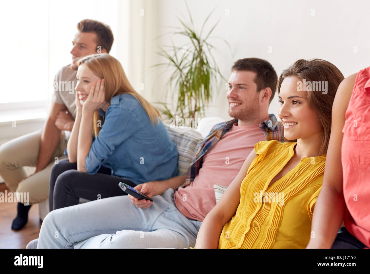 Heureux avec des amis à la maison à regarder la télévision à distance Banque D'Images