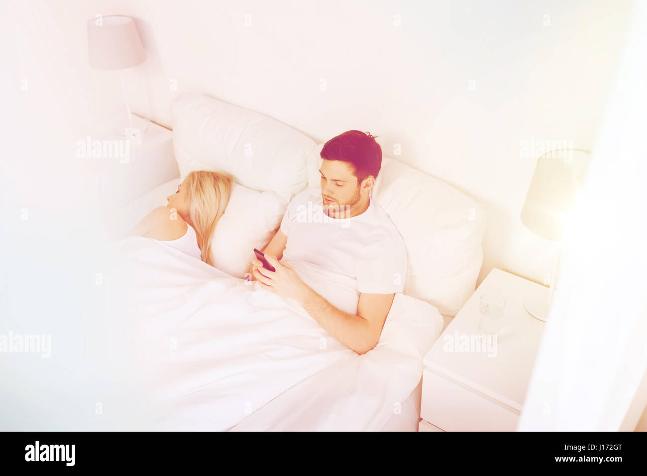 Man texting message tandis que la femme est sleeping in bed Banque D'Images