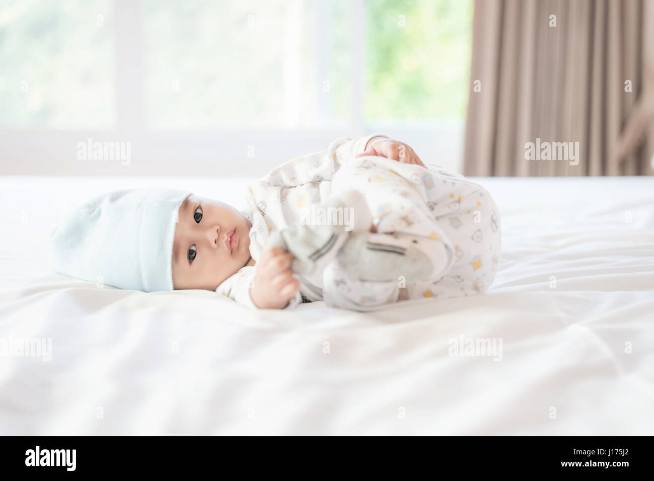 Portrait de 4 mois bébé asiatique et jouer le pied sur le lit dans la chambre blanche à la maison. Banque D'Images