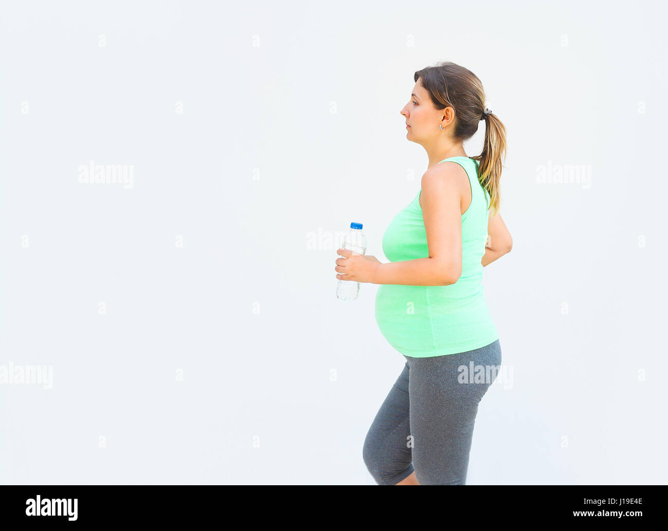 Jolie femme enceinte de faire des exercices de remise en forme en plein air avec bouteille d'eau potable Banque D'Images