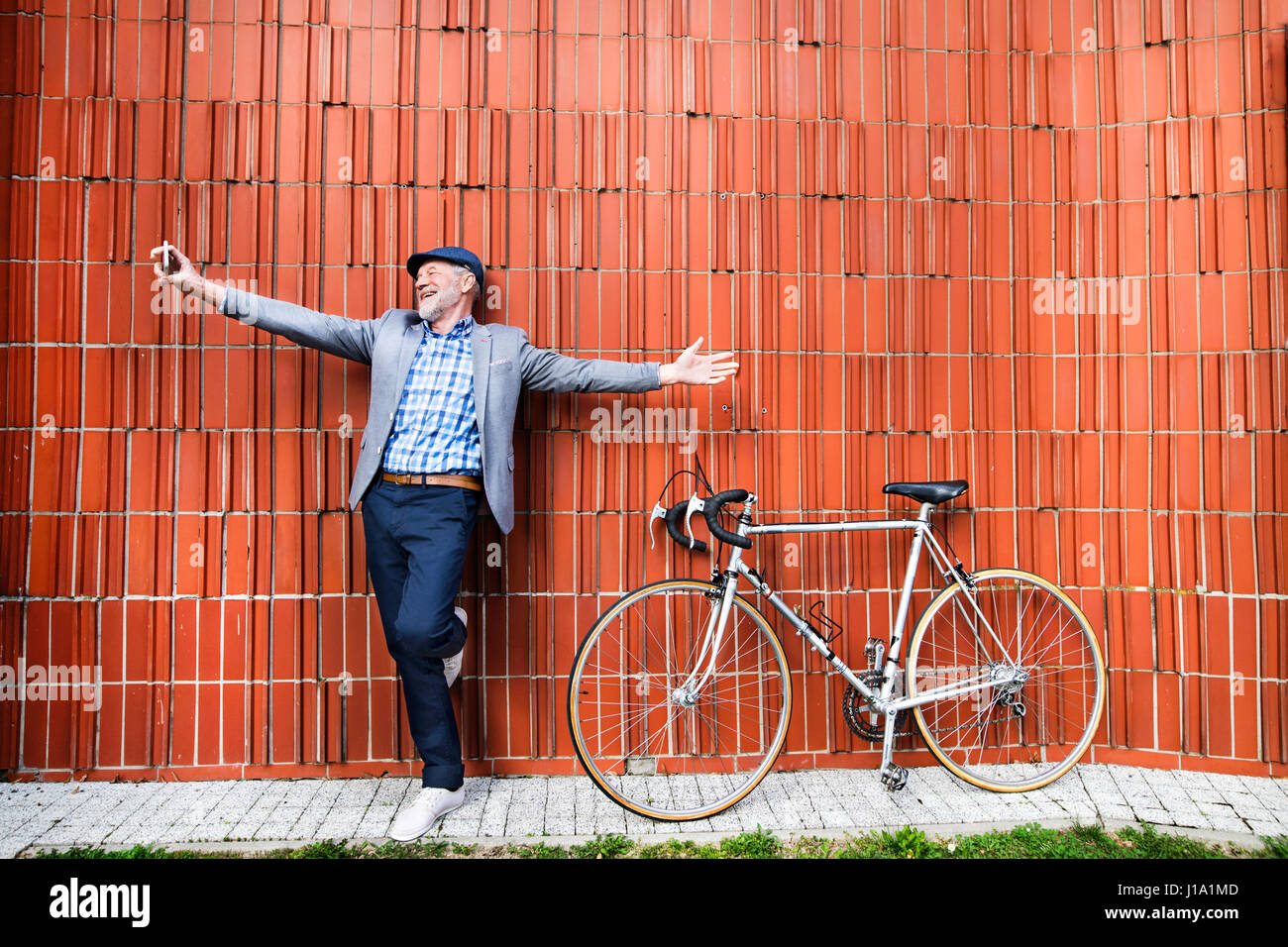 Handsome man chemise à carreaux bleu et gris veste avec location holding smart phone, en tenant. selfies Mur de brique Orange Arrière-plan. Banque D'Images