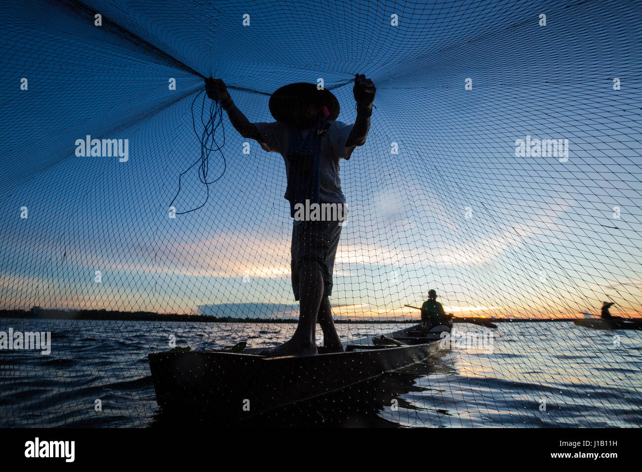 Thai Fisherman sur bateau en bois jetaient un filet pour attraper les poissons d'eau douce dans la rivière de la nature en début de soirée avant le coucher du soleil Banque D'Images