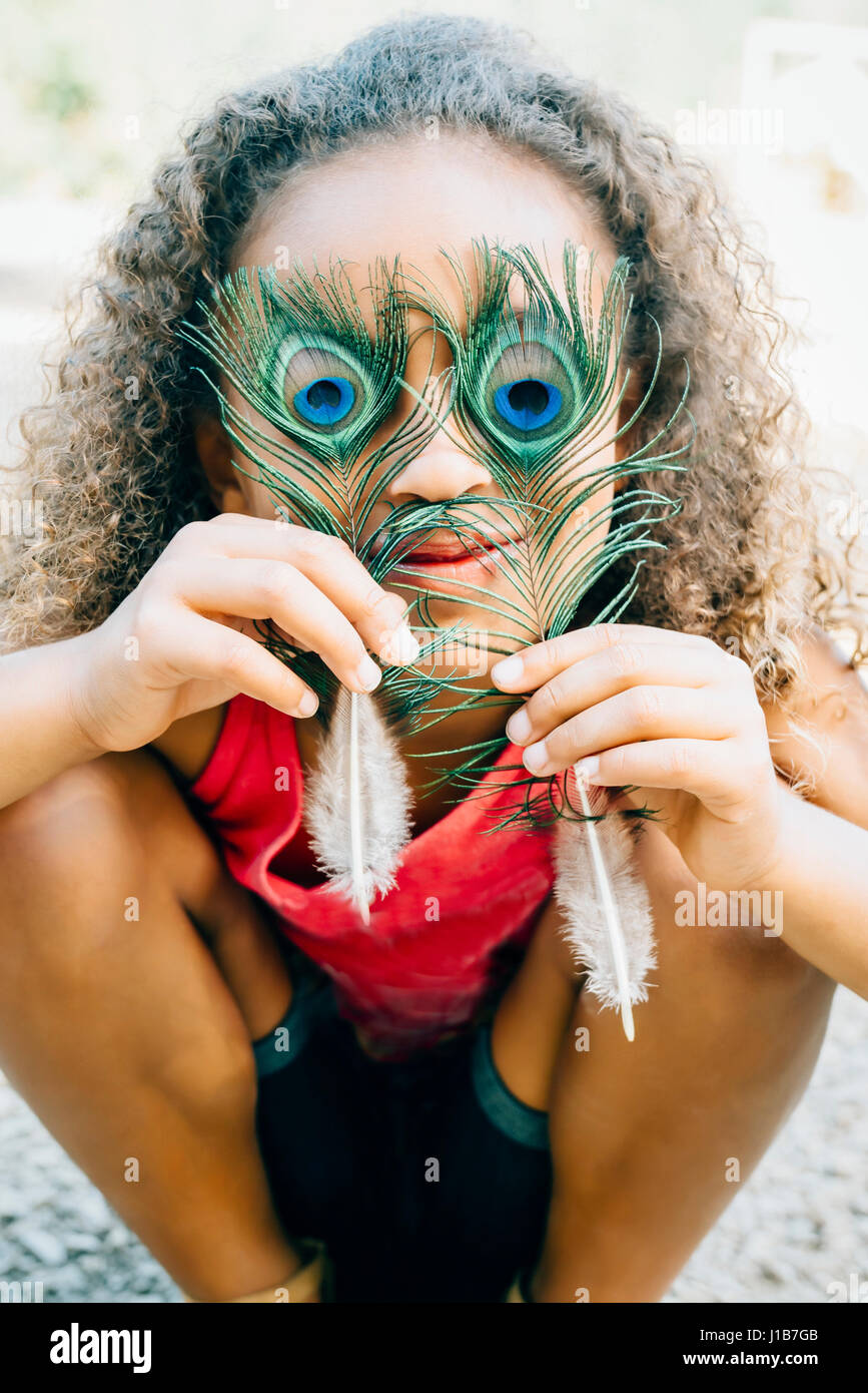 Mixed Race girl couvrant les yeux avec des plumes de paon Banque D'Images