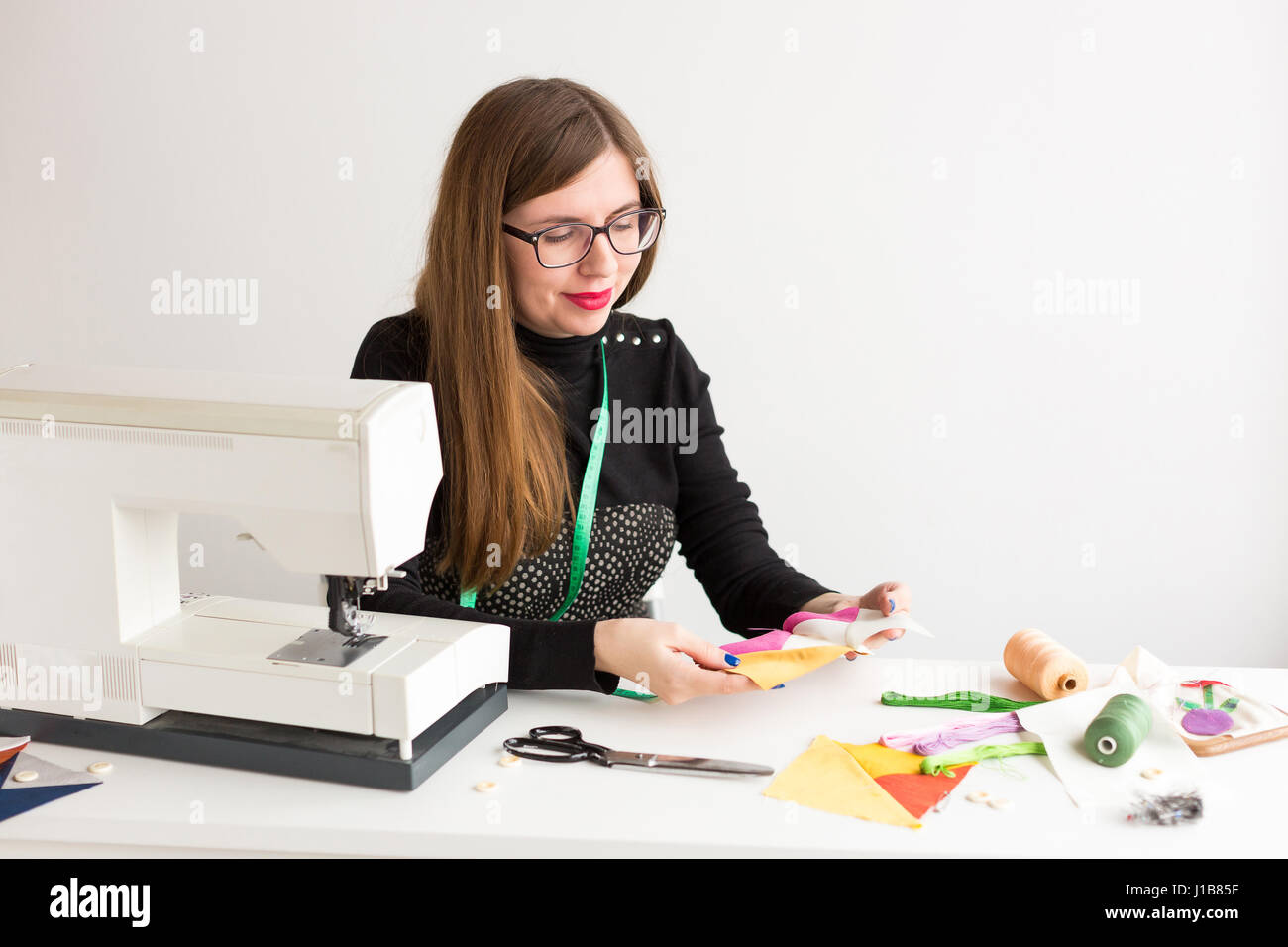 De couture et de quilting à la main dans l'atelier d'une jeune femme, d'un tailleur sur fond blanc - young smiling woman adapter tient dans ses mains cousus sur la machine à coudre les morceaux de tissus colorés Banque D'Images