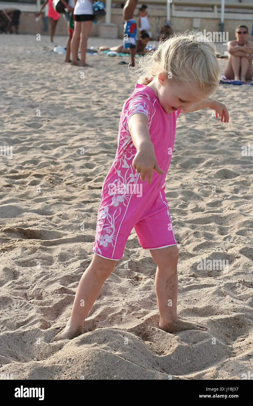 Petite fille, enfant avec une tresse française dans ses cheveux ont  beaucoup de plaisir à jouer sur la plage, le sable des coups, le port d'un  maillot de corps complet, onesie Photo