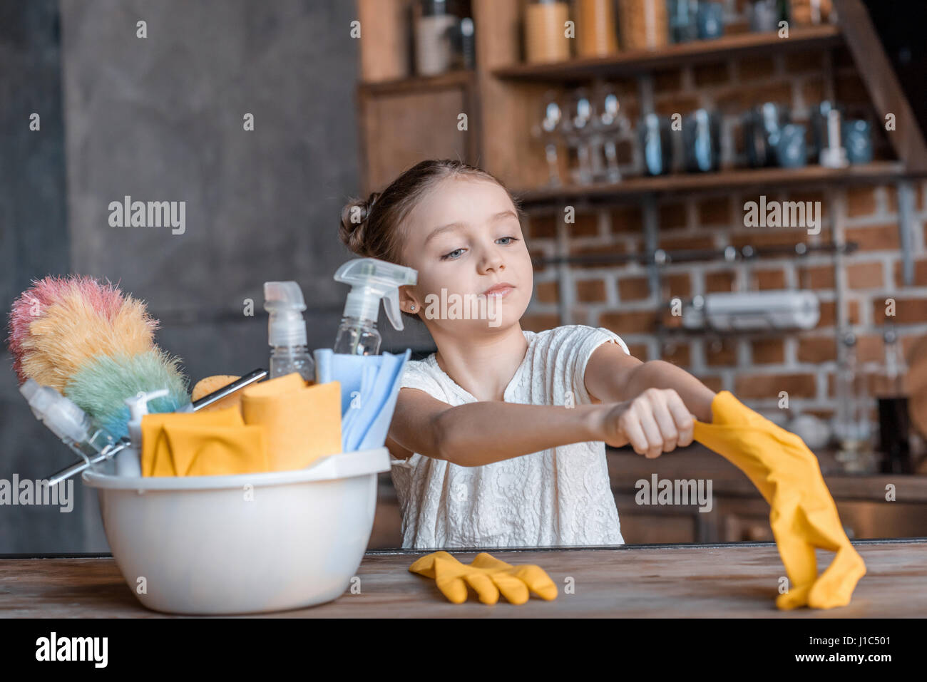 Adorable fille avec des gants de caoutchouc et de différents produits de nettoyage à la maison Banque D'Images