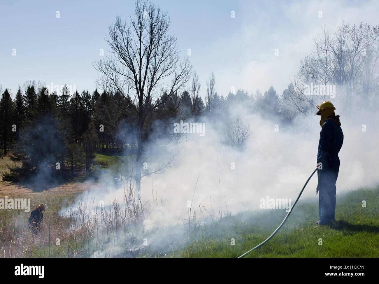 Une personne de la gravure d'un domaine alors qu'un autre s'en tient avec un tuyau d'eau. Banque D'Images