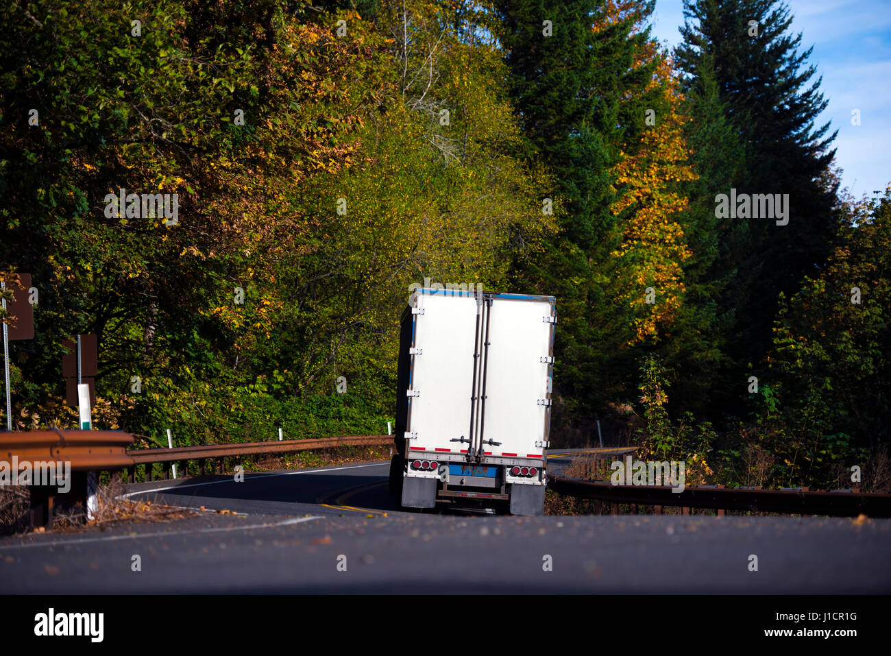 Paysage de la route sinueuse, en passant par la forêt d'automne avec arbres jaunies, avec une barrière de sécurité en métal et un contrastée à fond jaune et vert Banque D'Images