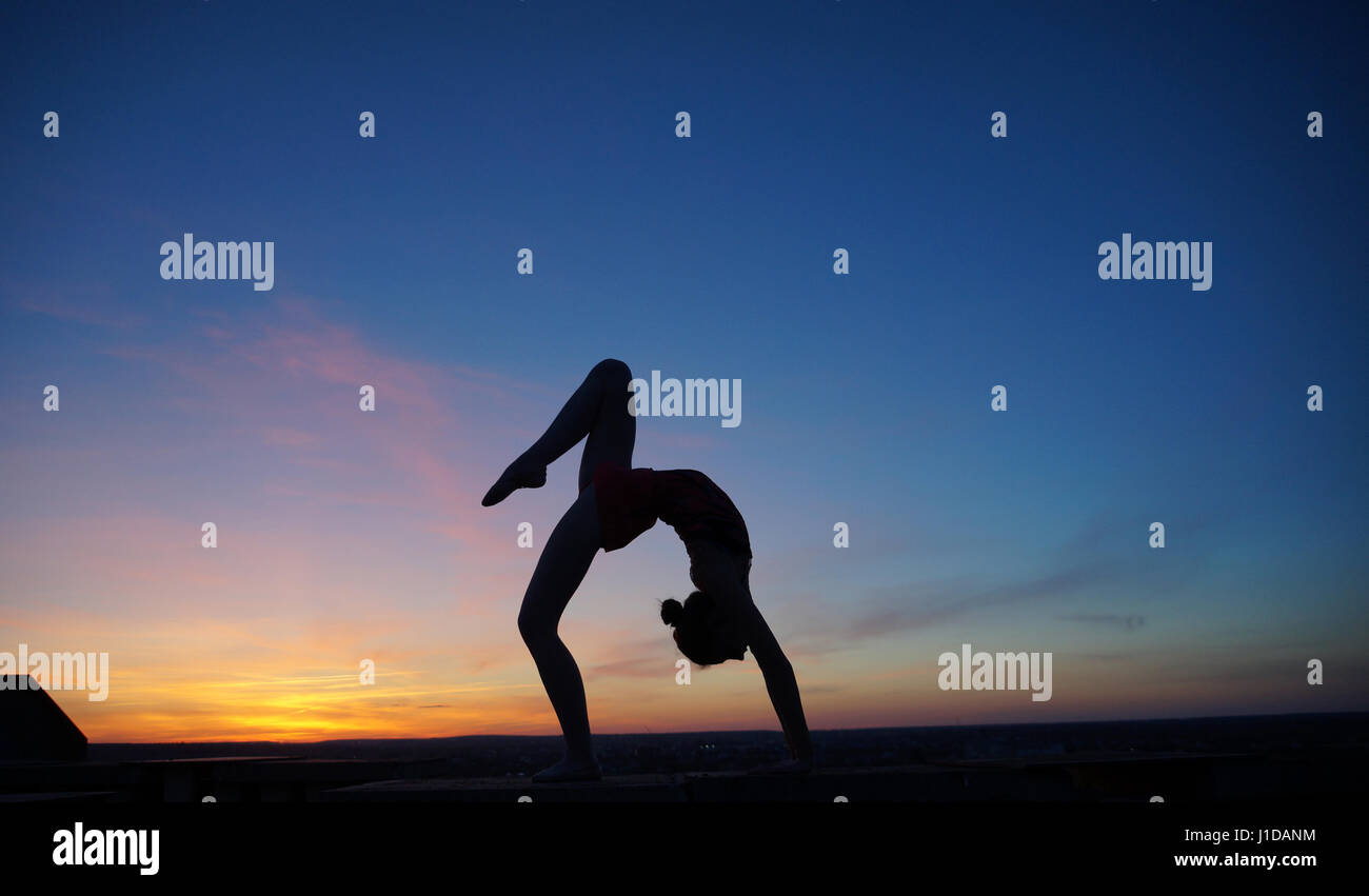 Danseuse dans la dance ne le divise dans l'air contre le coucher du soleil Banque D'Images