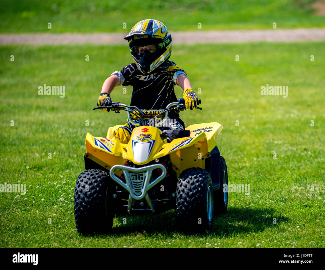 Jeune garçon sur quatre roues quad avec casque dans la conduite de l'herbe Banque D'Images