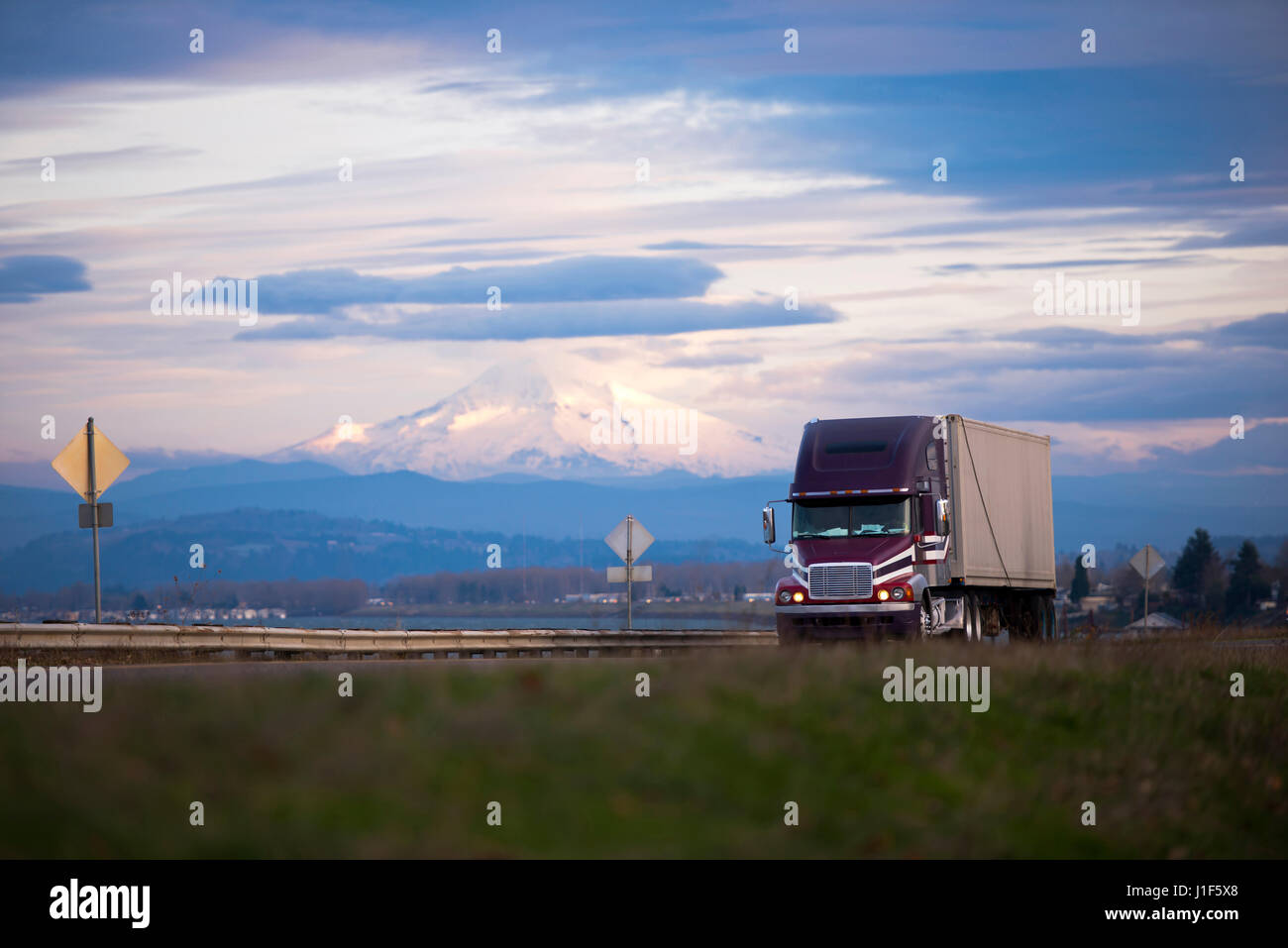 Camion semi professionnel sombre avec remorque Transport de marchandises commerciales sur la pittoresque route avec une barrière de sécurité en métal sur l'arrière-plan de Mount Hood Banque D'Images