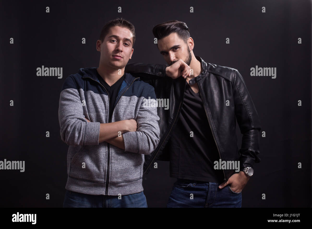 Deux jeunes hommes adultes, pose, des vêtements décontractés. Fond noir, studio. Banque D'Images