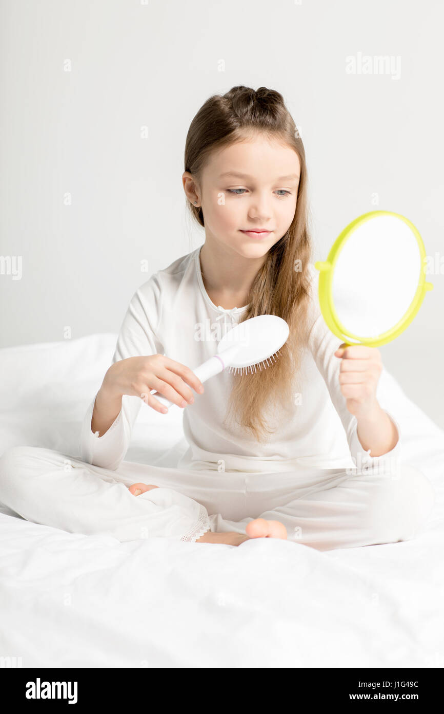 Adorable petite fille en pyjama assis sur le lit et peigner les cheveux Banque D'Images