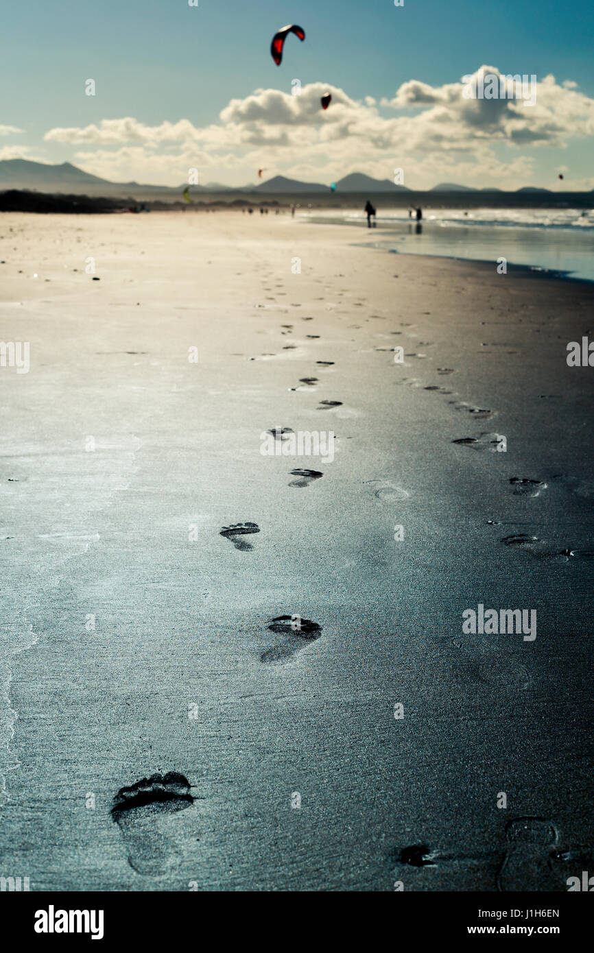 De gros plan des traces de pas dans le sable de la plage de Famara Lanzarote, Canaries, Espagne, avec quelques kitesurfers dans l'arrière-plan Banque D'Images