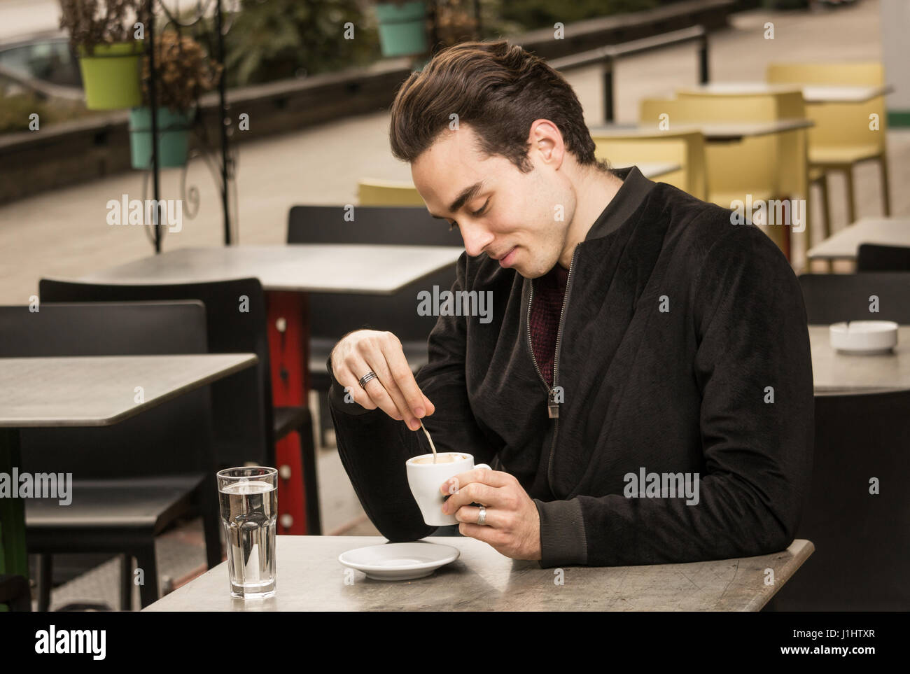 Un jeune homme adulte, à la tasse de café, à la cuillère, en remuant à l'extérieur jour Banque D'Images