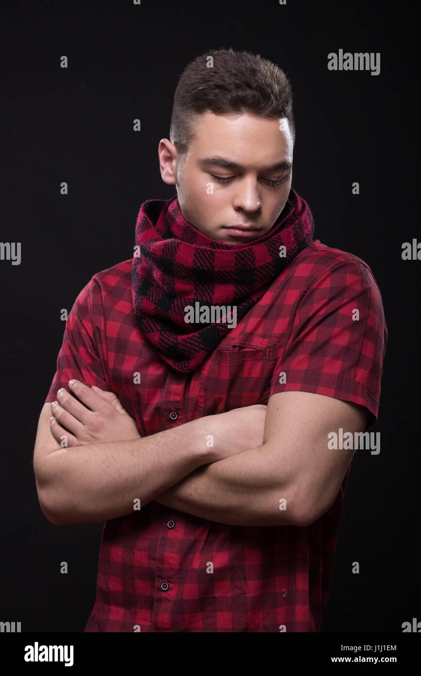 Un jeune adulte homme insatisfait, regardant vers le bas, haut du corps,  les bras, le foulard rouge, fond noir Photo Stock - Alamy