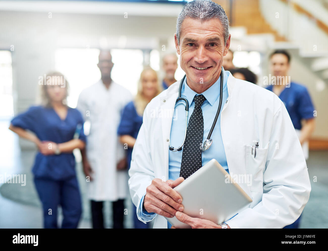 Médecin positive avec la tablette et en regardant la caméra. Comité permanent de l'équipe médicale en arrière-plan Banque D'Images