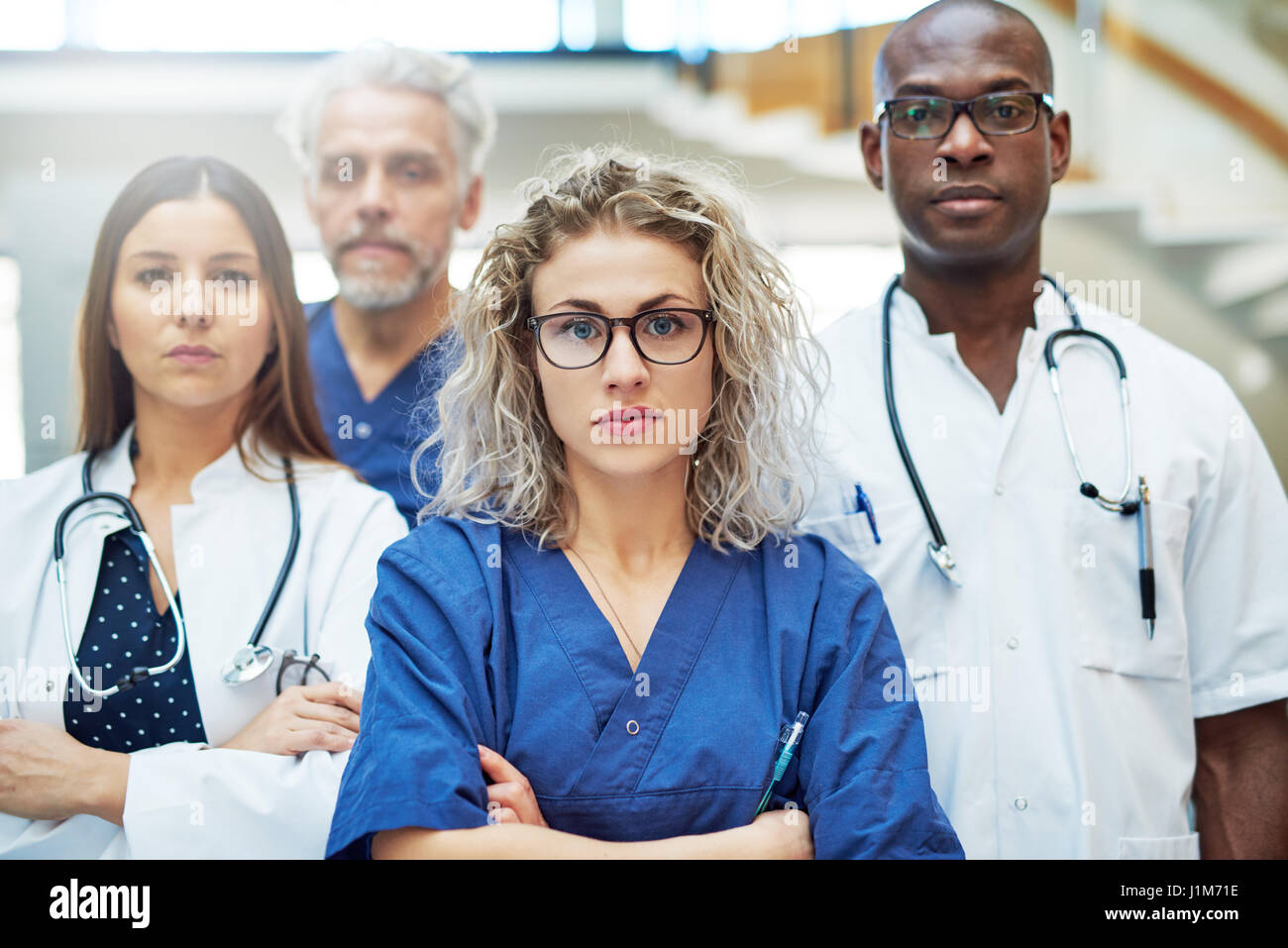 L'équipe de médecins sérieux looking at camera debout dans une clinique. Les médecins de l'équipe de courses mixtes Banque D'Images