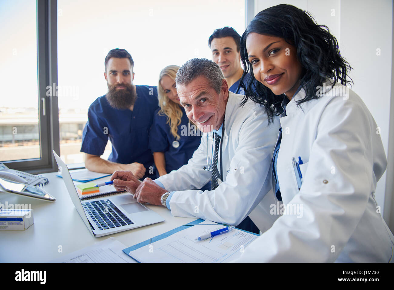 L'équipe de positive de doctors standing at desk smiling to camera alors que j'assistais à une réunion Banque D'Images
