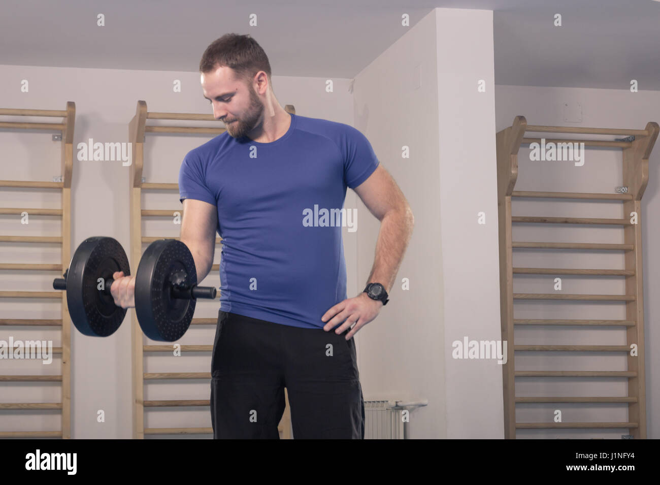 Seulement, un jeune homme confiant, exercice musculaire encombrant grand un haltère, à l'intérieur Banque D'Images