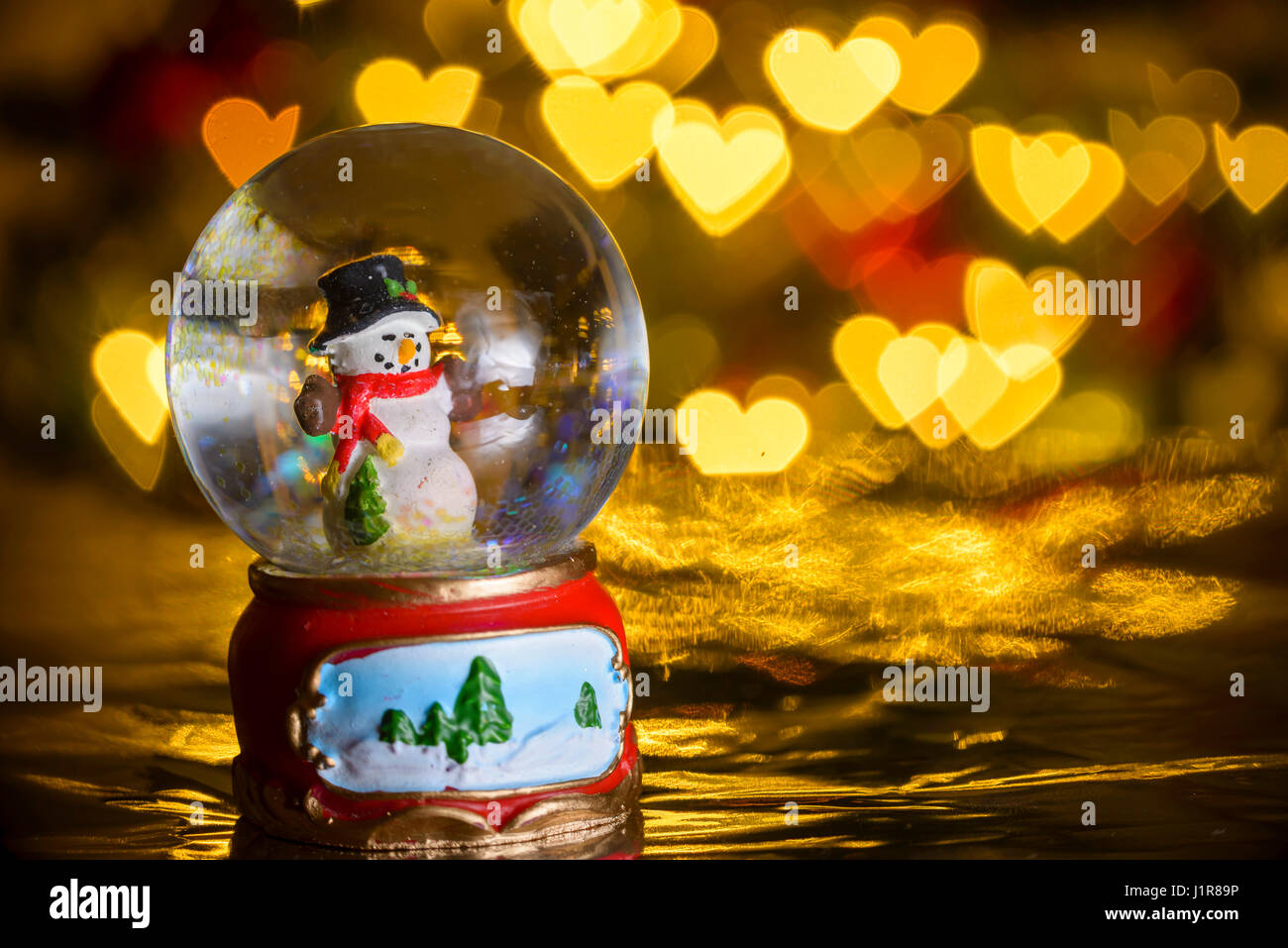 Boule à neige de Noël avec des lumières de Noël en arrière-plan ; bonhomme avec présente ; coeur de formes, blur bokeh Banque D'Images