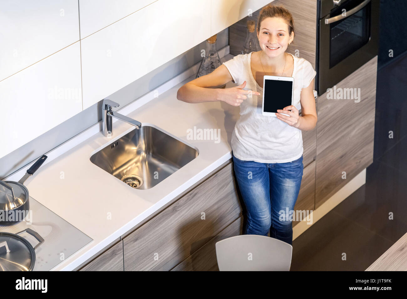 Belle Jeune femme tenant le comprimé dans la cuisine et l'écran montrant avec le doigt et sourire à pleines dents à l'appareil photo. Banque D'Images