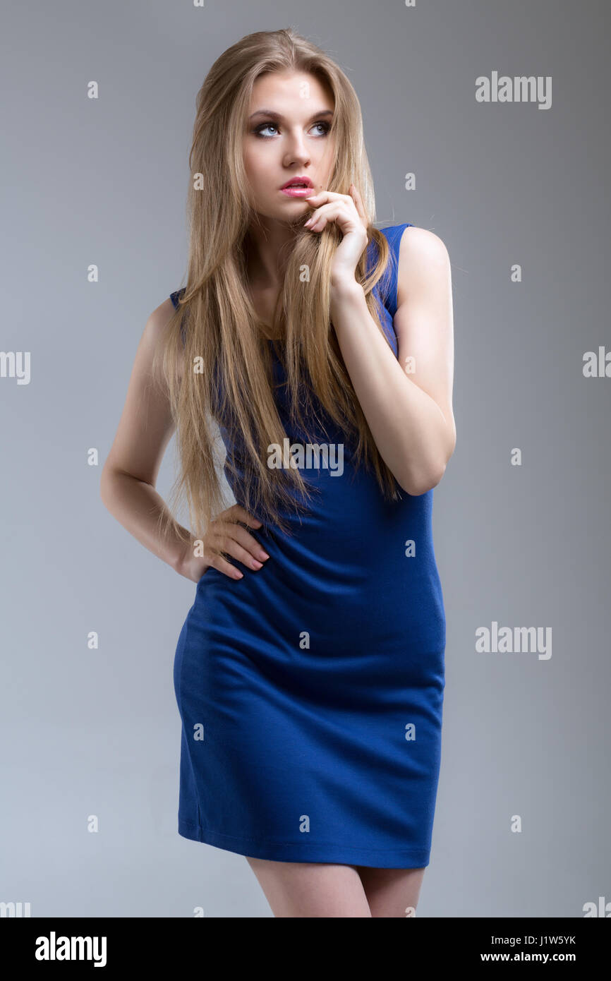 Blonde aux cheveux longs à la mode dans une robe bleue sur fond gris Banque D'Images