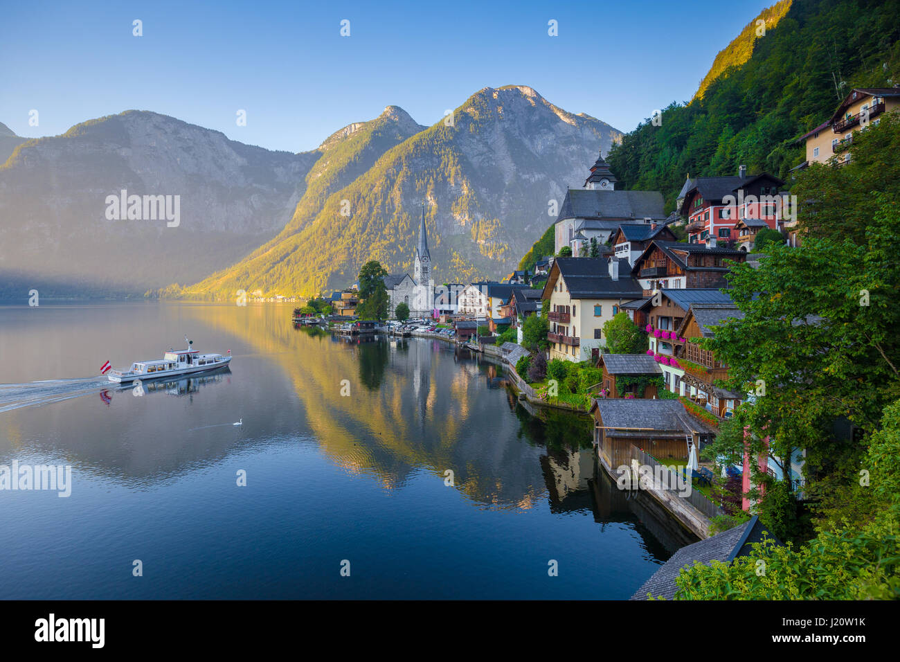 Vue de carte postale classique de la célèbre ville au bord du lac de Hallstatt dans les Alpes avec des passagers à bord d'un navire traditionnel au début de lumière du matin à l'aube, Autriche Banque D'Images