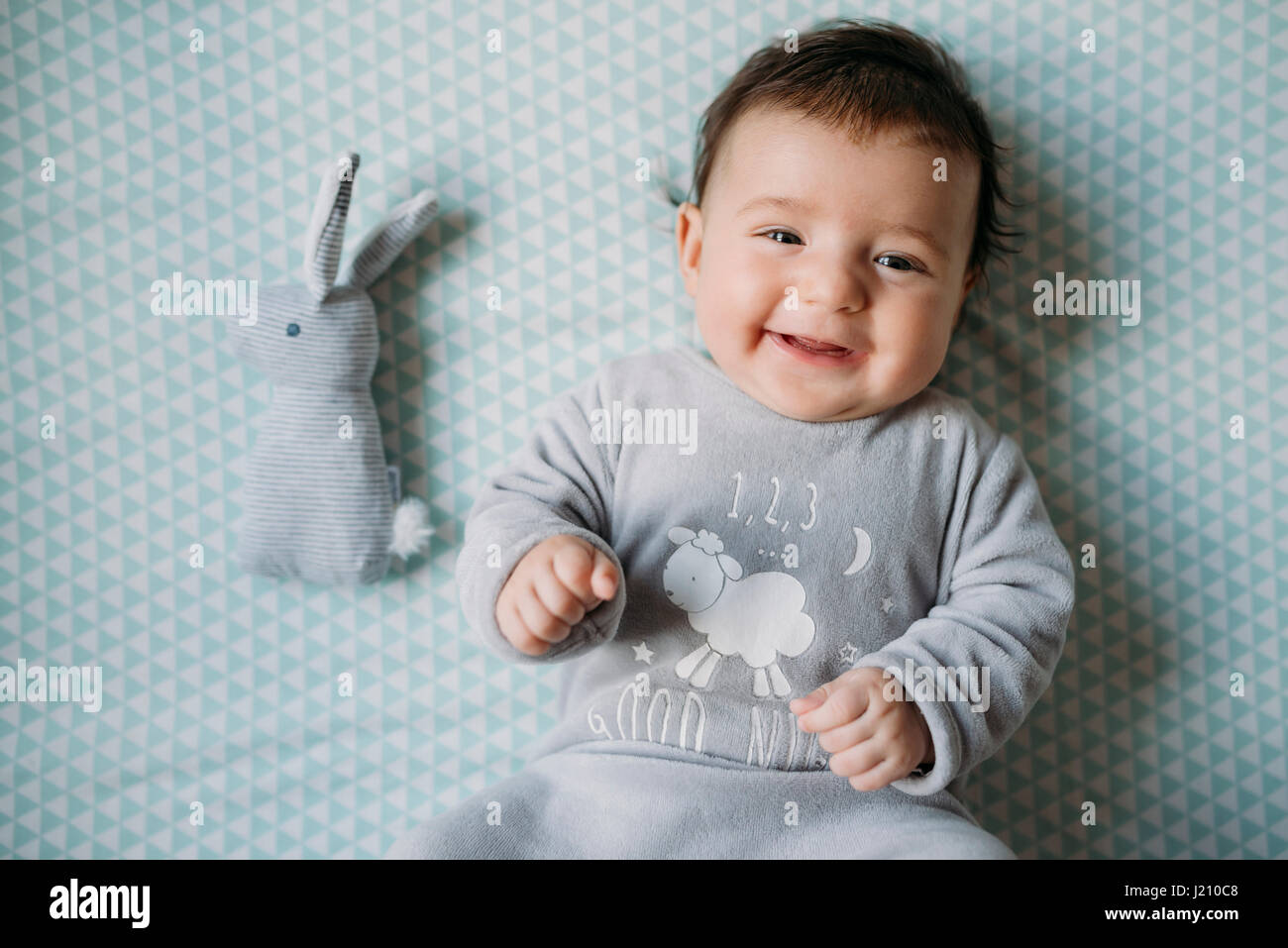 Portrait of smiling baby girl lying on lit à côté de toy bunny Banque D'Images
