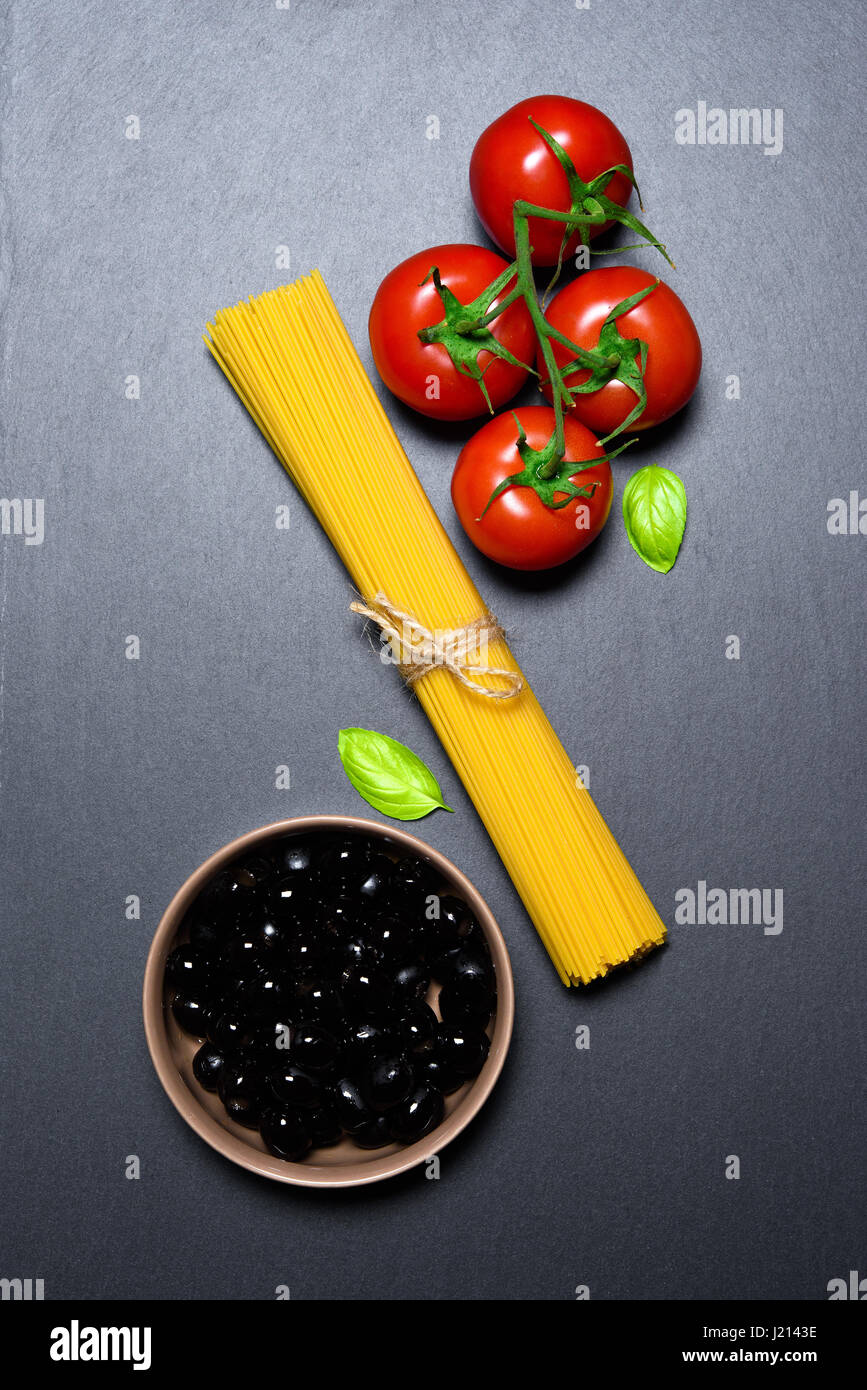 Vue d'en haut : les pâtes italiennes ou spaghetti, tomates, olives et l'origan sur fond ardoise noire Banque D'Images