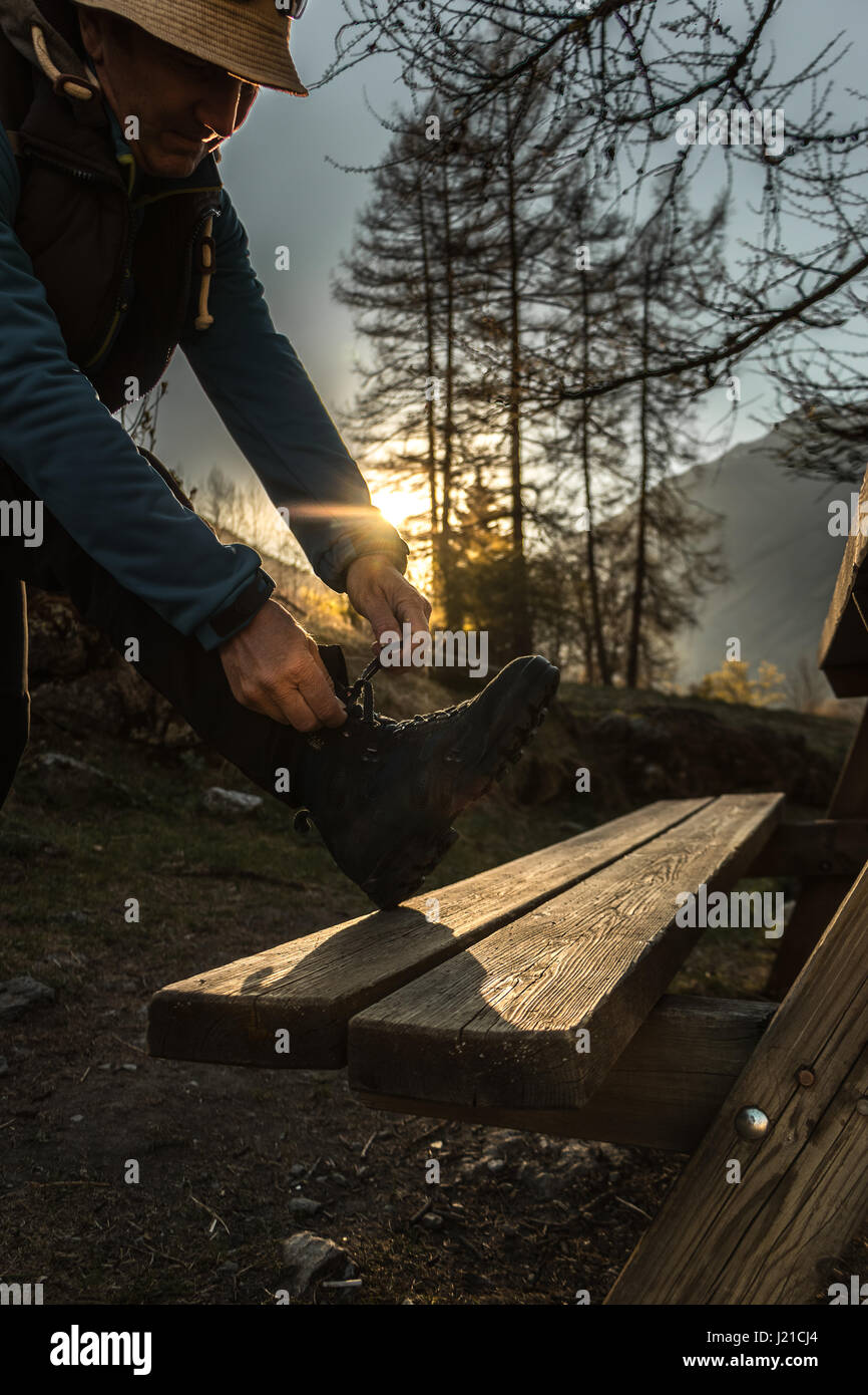 Un homme s'adapter ses chaussures de randonnée pour aller pour une randonnée de montagne comme le lever ou le coucher du soleil dans les montagnes des Alpes arbres paysage alpin Vanoise National Park Banque D'Images