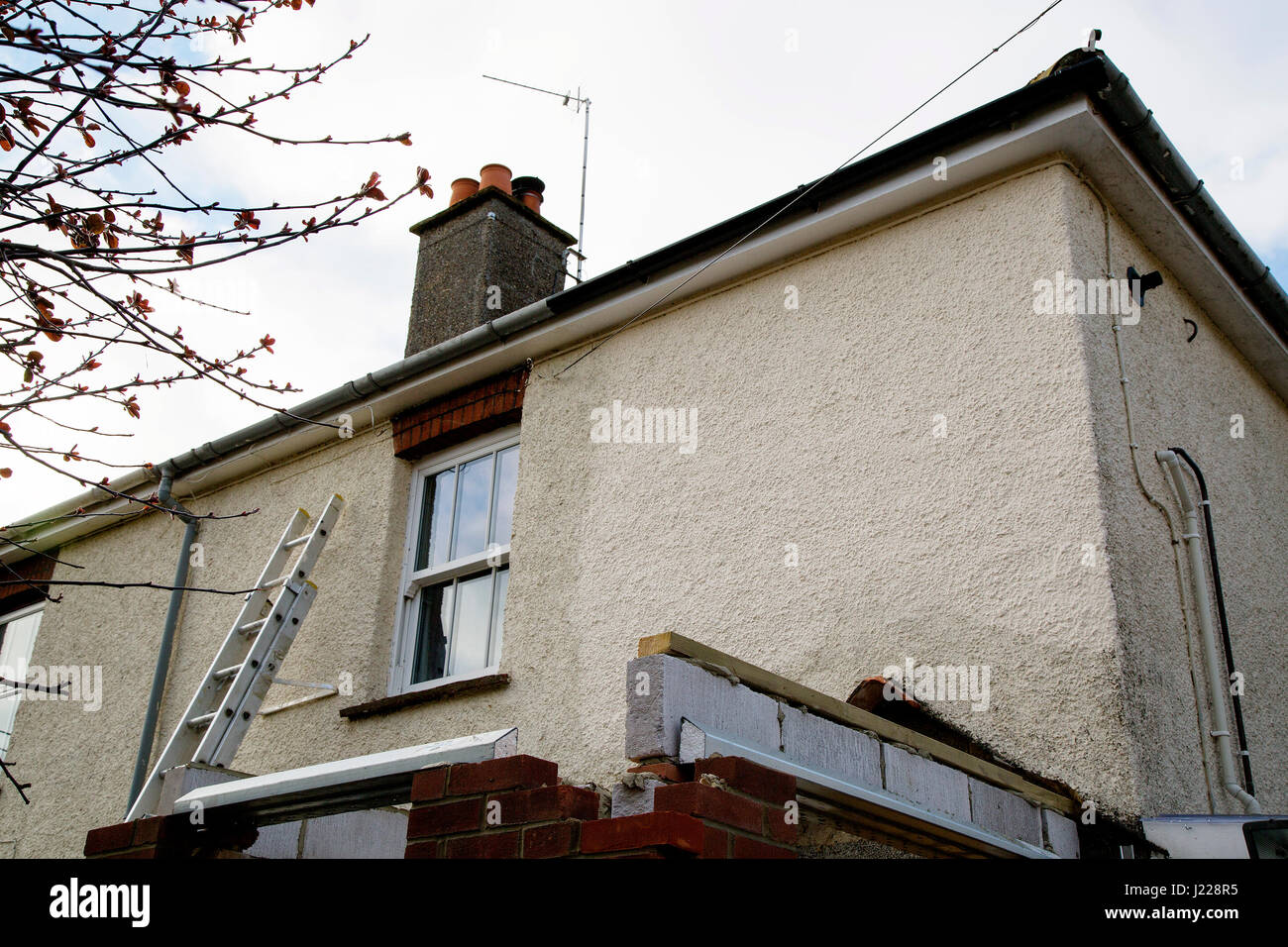 Travaux de rénovation en cours sur une partie de maison avec façade rendue et à construire une véranda. Une échelle s'appuie contre le mur. Banque D'Images