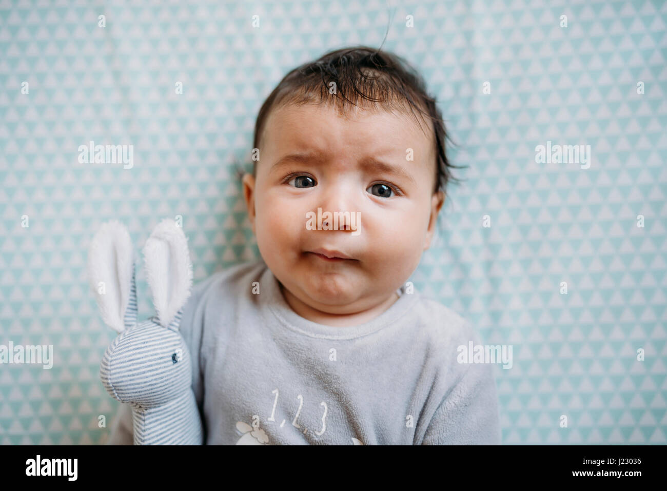 Portrait of baby girl lying on bed with toy bunny pulling funny face Banque D'Images
