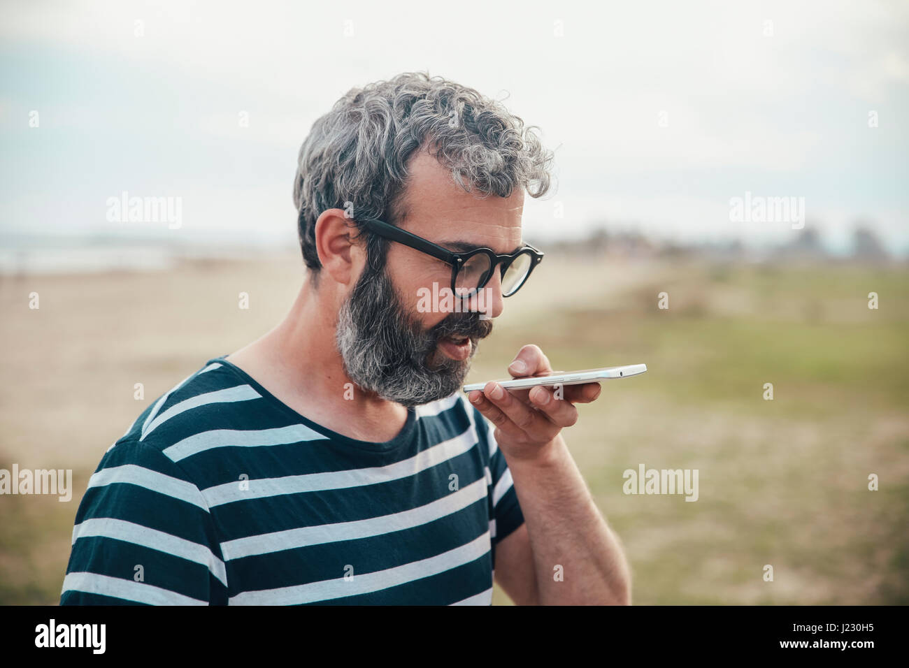 Homme barbu envoyer un message avec le smartphone sur la plage Banque D'Images