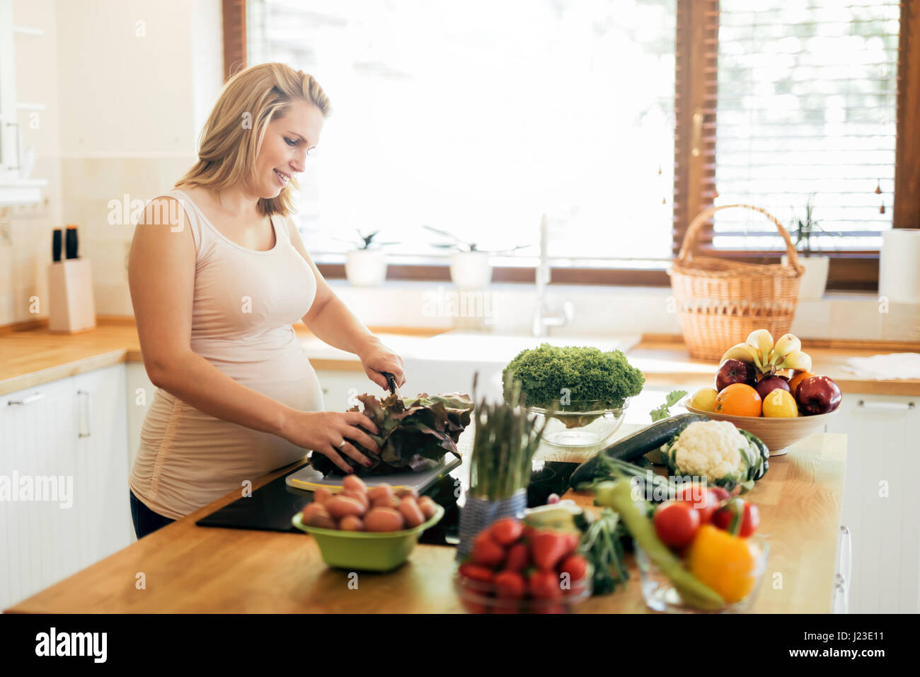 Belle femme enceinte, la préparation de repas sur l'île de cuisine à partir de produits frais Banque D'Images