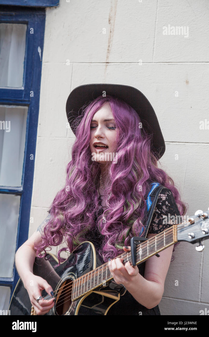 Une jeune femme avec de longs cheveux violets busker,chantant et jouant de la guitare à l'Whitby Goth Week-end à North Yorkshire, Angleterre, Royaume-Uni Banque D'Images