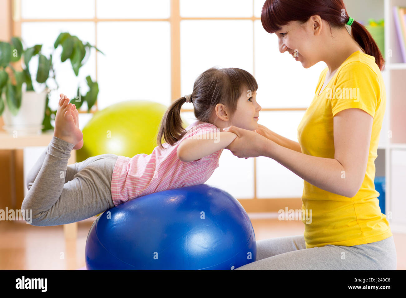 Enfant girl doing gymnastic sur fitness ball avec la mère à la maison Banque D'Images