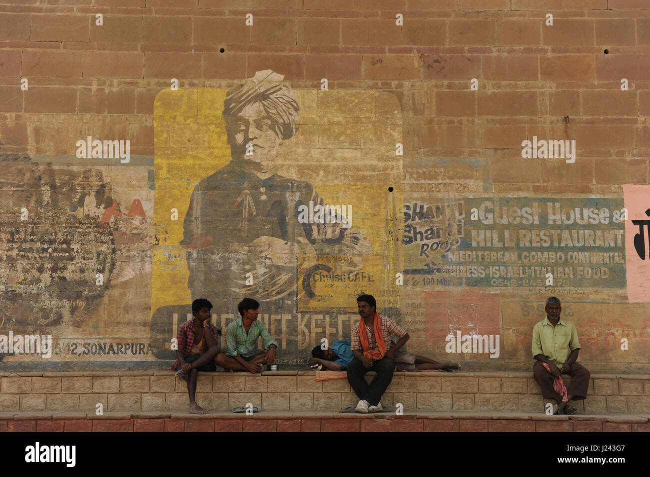 Cinq hommes reste par un mur sur lequel la publicité en couleurs montre pour hôtels, cafés et restaurants à Varanasi, Inde, Uttar Pradesh Banque D'Images