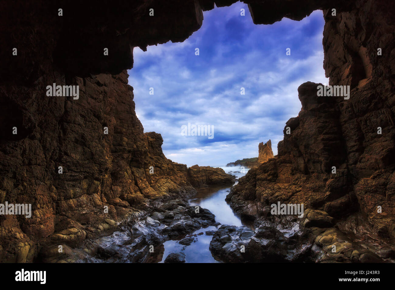 Grotte rocheuse vers la mer ouverte au coucher du soleil près de la plage et des rochers de la cathédrale Bombo de Pacific Coast en Australie. Banque D'Images