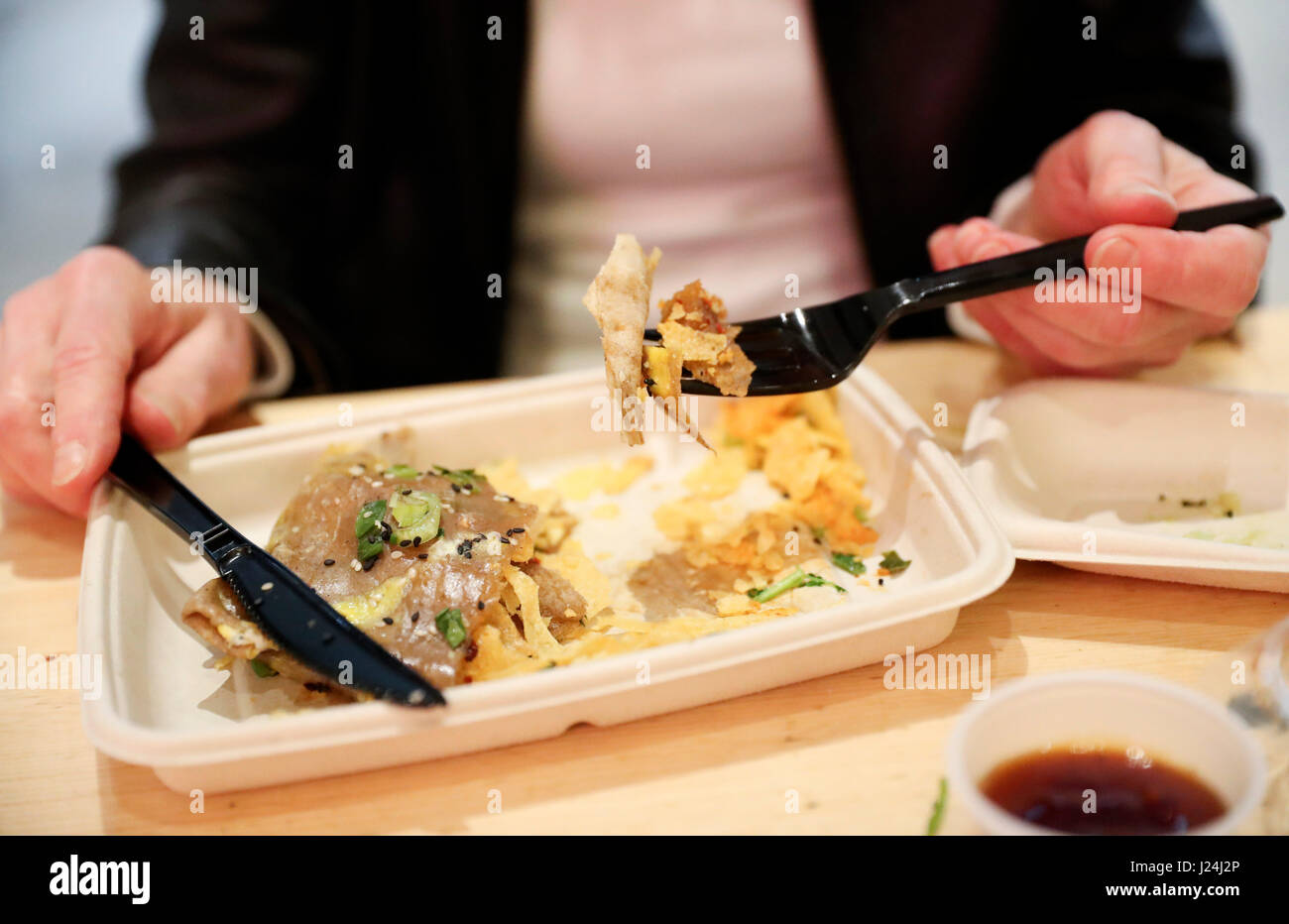 New York, USA. Apr 25, 2017. Un client a de M. Jianbing Bing dans UrbanSpace food court à New York, États-Unis, 17 avril 2017. UrbanSpace en plein centre de New York est un endroit blanc-colliers viennent pour le déjeuner pendant leurs journées de travail. Depuis quelques mois, les clients ont toujours la queue devant un kiosque sous une bannière avec les caractères chinois. Ce que ce kiosque vend est une cuisine chinoise authentique dans le nord de la Chine -- Jianbing, ou le crêpe de Chine. Source : Xinhua/Alamy Live News Banque D'Images