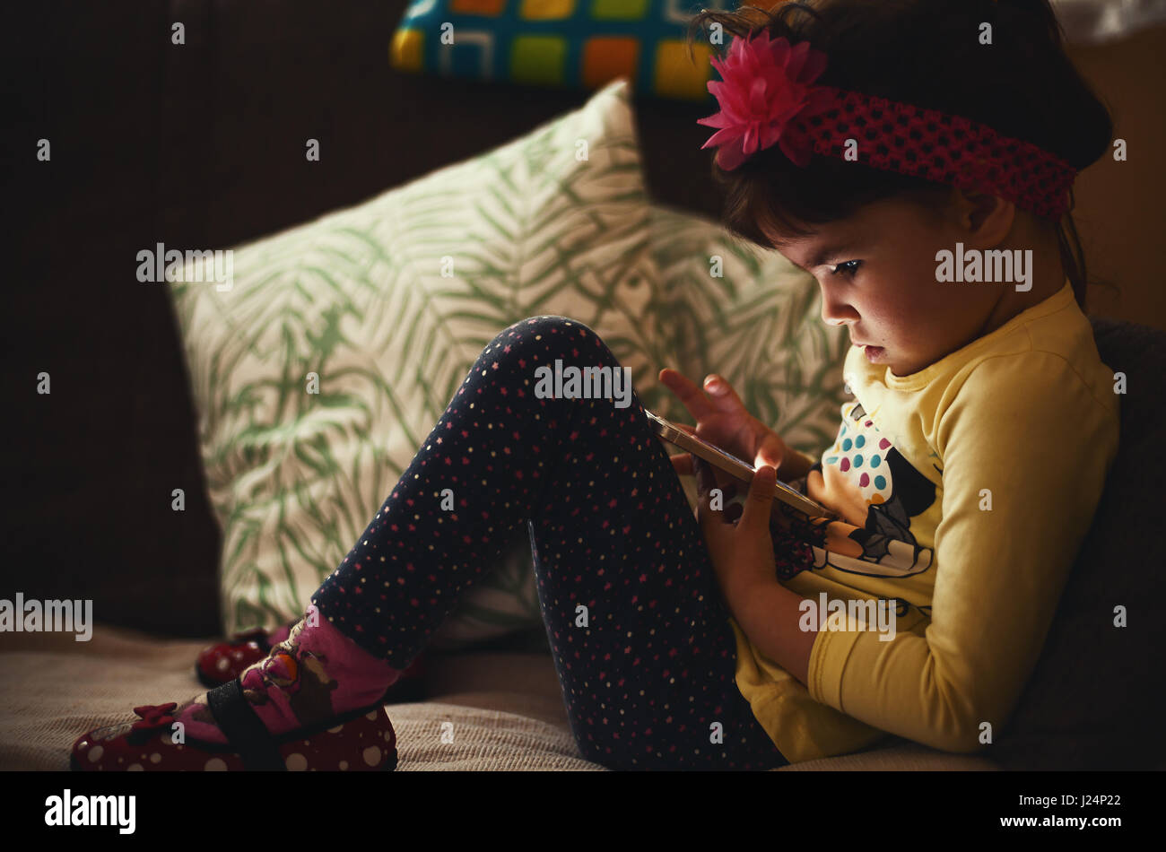 Petite fille est assise sur le canapé et regarder un téléphone mobile. Banque D'Images