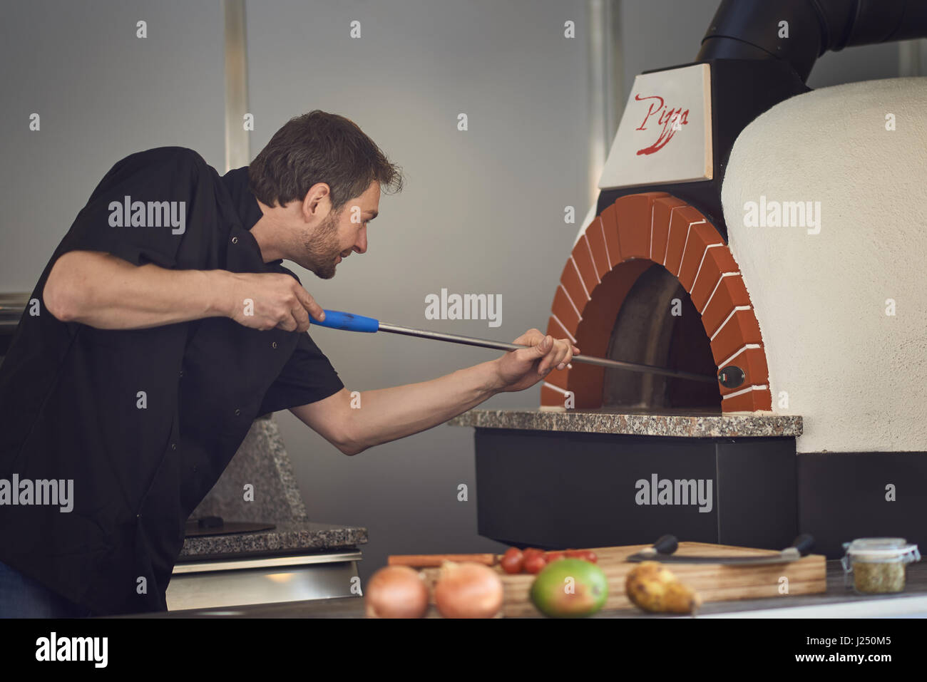 Chef d'âge moyen ou de cuisson Cuisson flamme une pizza italienne dans un four en pierre moderne à une pizzeria Banque D'Images