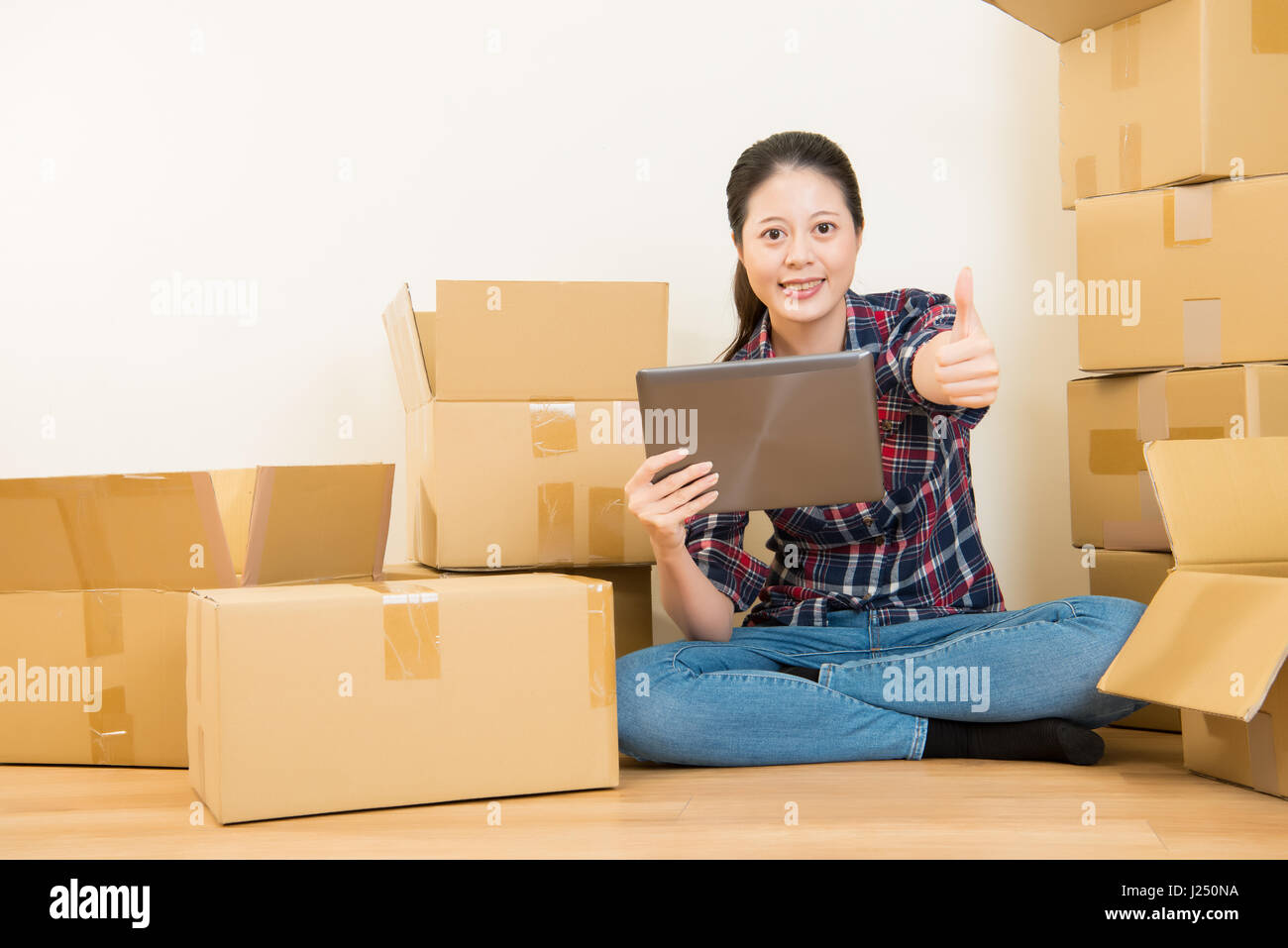 Heureux coup de pouce pour aller de maison avec beaucoup de boîtes de carton à l'aide de tablette numérique à la recherche. race mixte modèle chinois asiatique. Banque D'Images