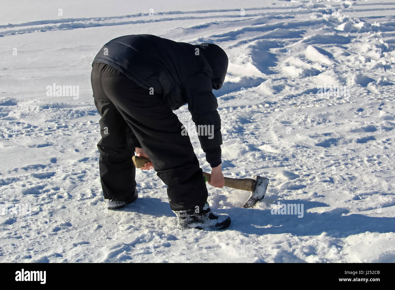 Hacher dans un vieux trou de pêche sur glace avec une hache. Banque D'Images